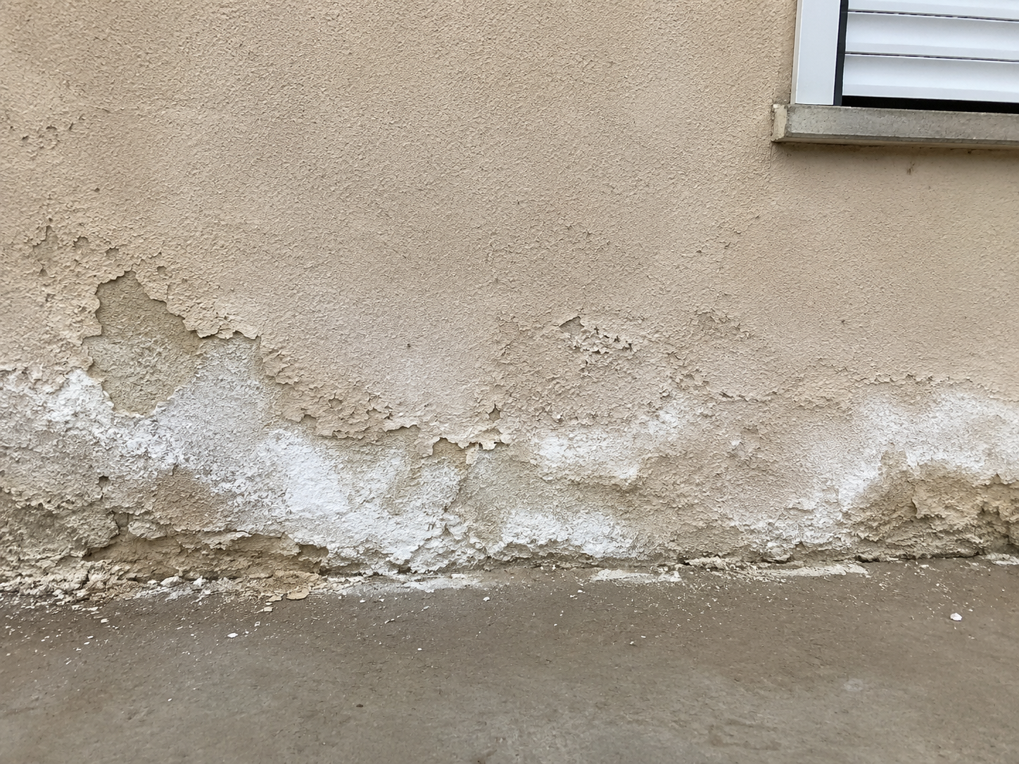 Signes d'un crépi qui s'effrite : aspect poudreux et taches blanches en bas de mur